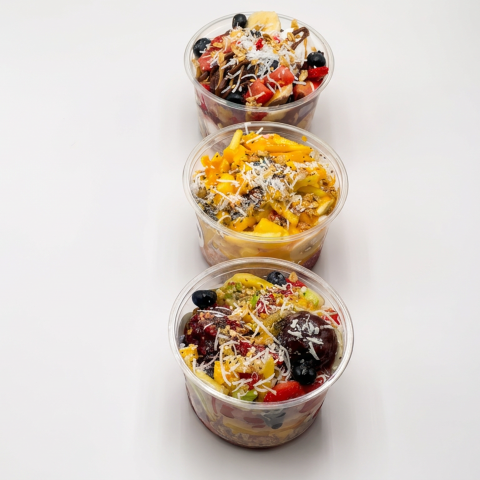 Three clear cups of colorful layered fruit topped with berries, shredded coconut, and drizzled sauce.